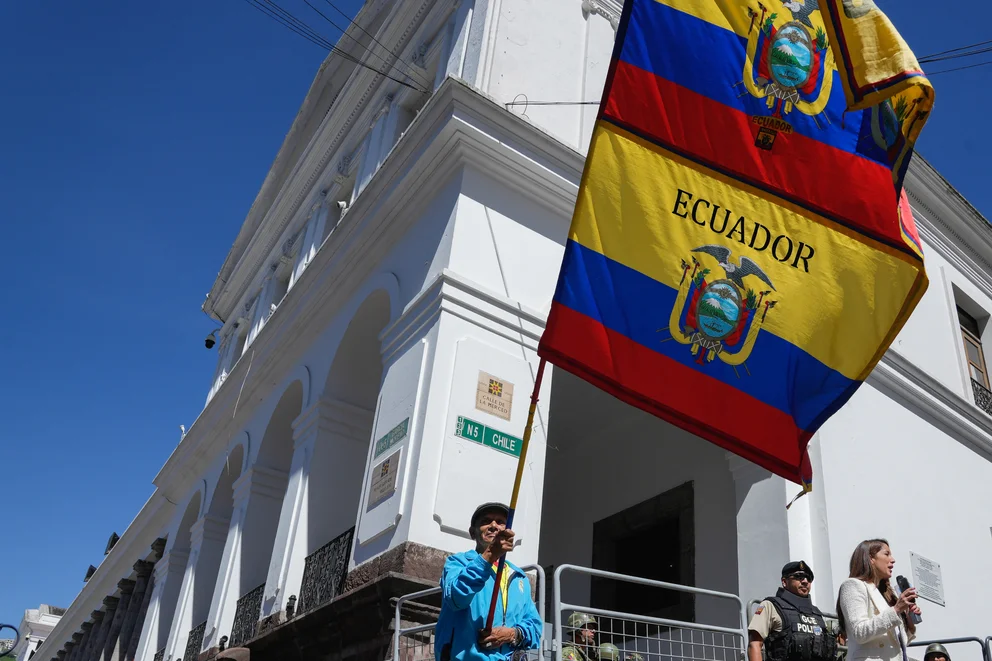Un hombre ondea las banderas nacionales de Ecuador frente al palacio presidencial